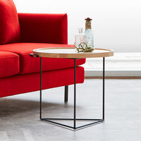 Round wooden side table with light wood top and black geometric metal legs, set against a bold red sofa.