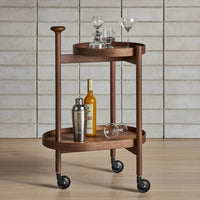 "Wooden bar cart in rich walnut finish with black wheels, featuring round trays and elegant glassware for stylish entertaining."