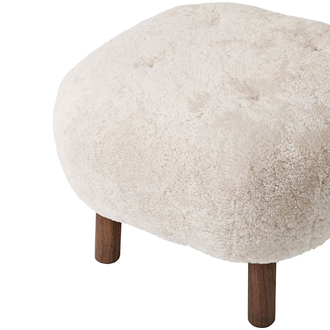 Cream-colored plush ottoman with a soft texture and wooden legs, featuring a simple, modern design.