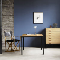 Light wood desk with a black frame, set against a blue wall and a textured gray brick background. Modern, minimalistic decor.