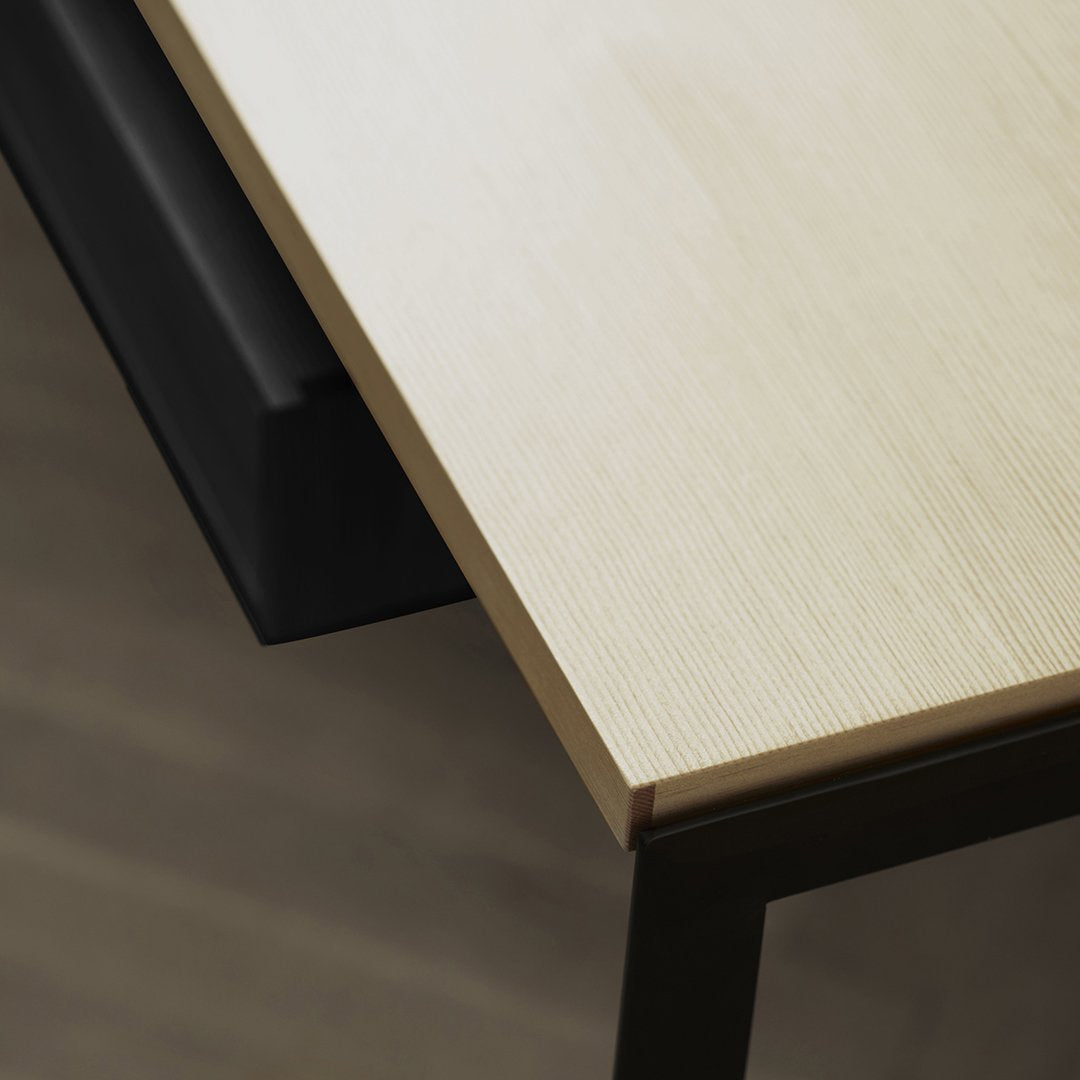 Light wood tabletop with a textured finish, contrasting with a sleek black drawer below.
