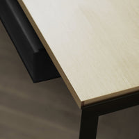 Light wood tabletop with a textured finish, contrasting with a sleek black drawer below.