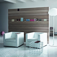 Modern white armchairs against a warm wood wall, complemented by a sleek metal table and soft lighting.