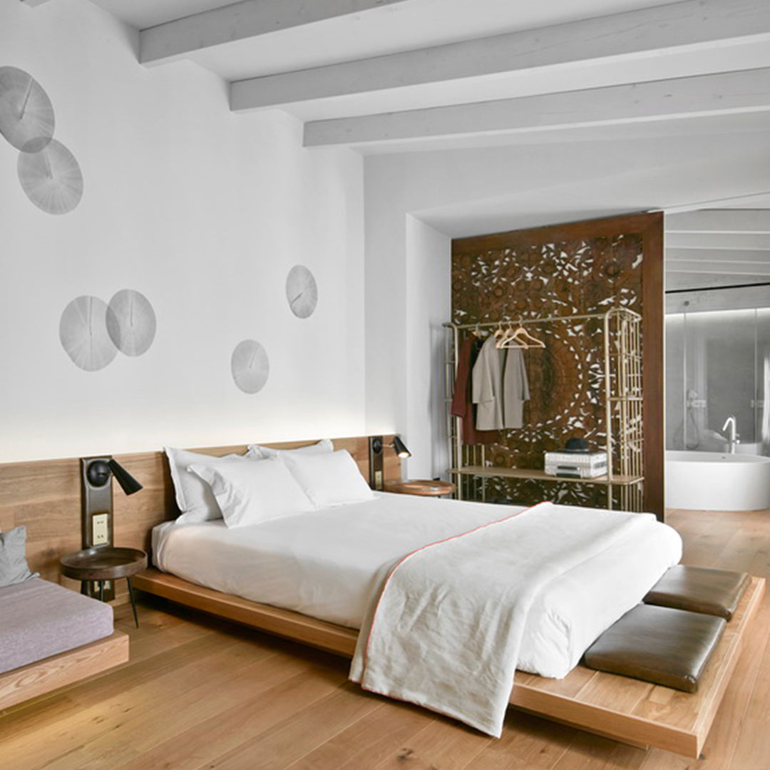 Sleek white bedspread with pale wood accents, gray pillows, and artistic wall patterns in a modern bedroom design.