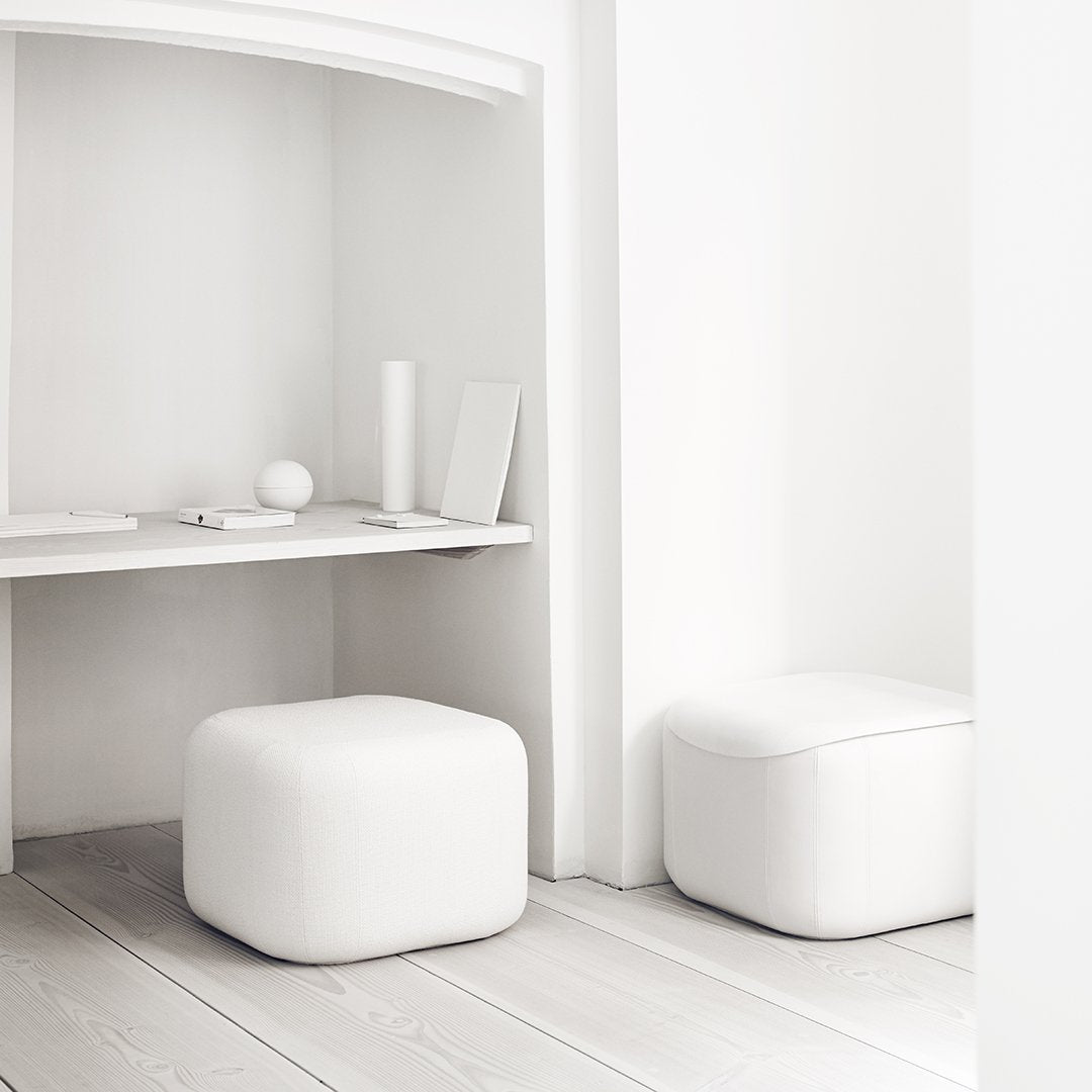 Two minimalist white ottomans in a bright, modern interior with light wooden flooring.