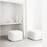 Two minimalist white ottomans in a bright, modern interior with light wooden flooring.