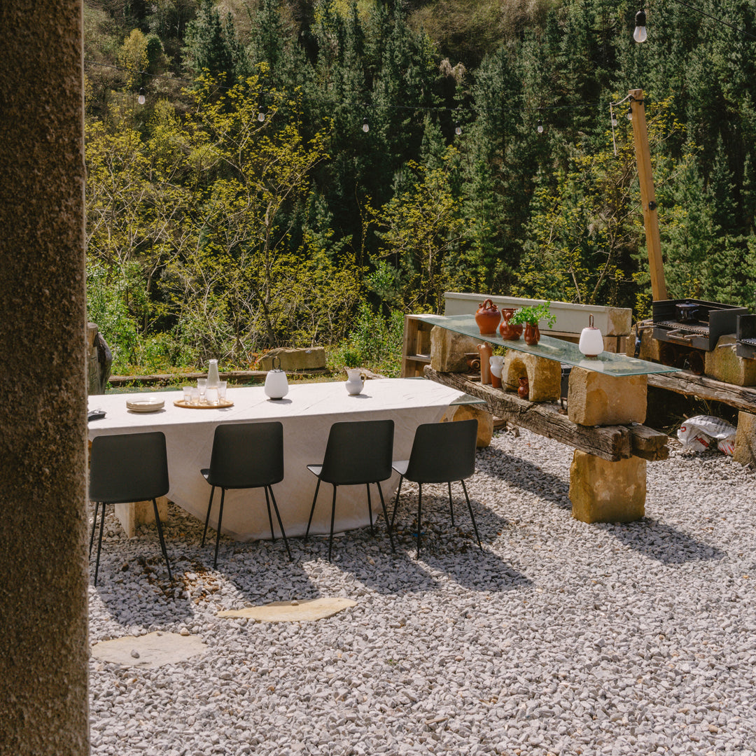Outdoor dining setup featuring a neutral tablecloth, black chairs, and natural stone elements amidst lush greenery.