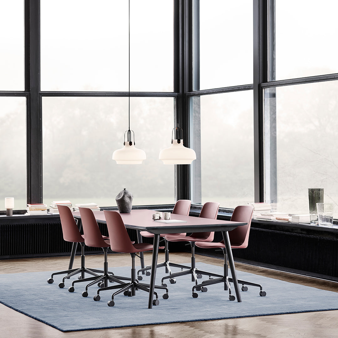 Modern workspace featuring pink ergonomic chairs on a soft blue rug beneath hanging light fixtures.