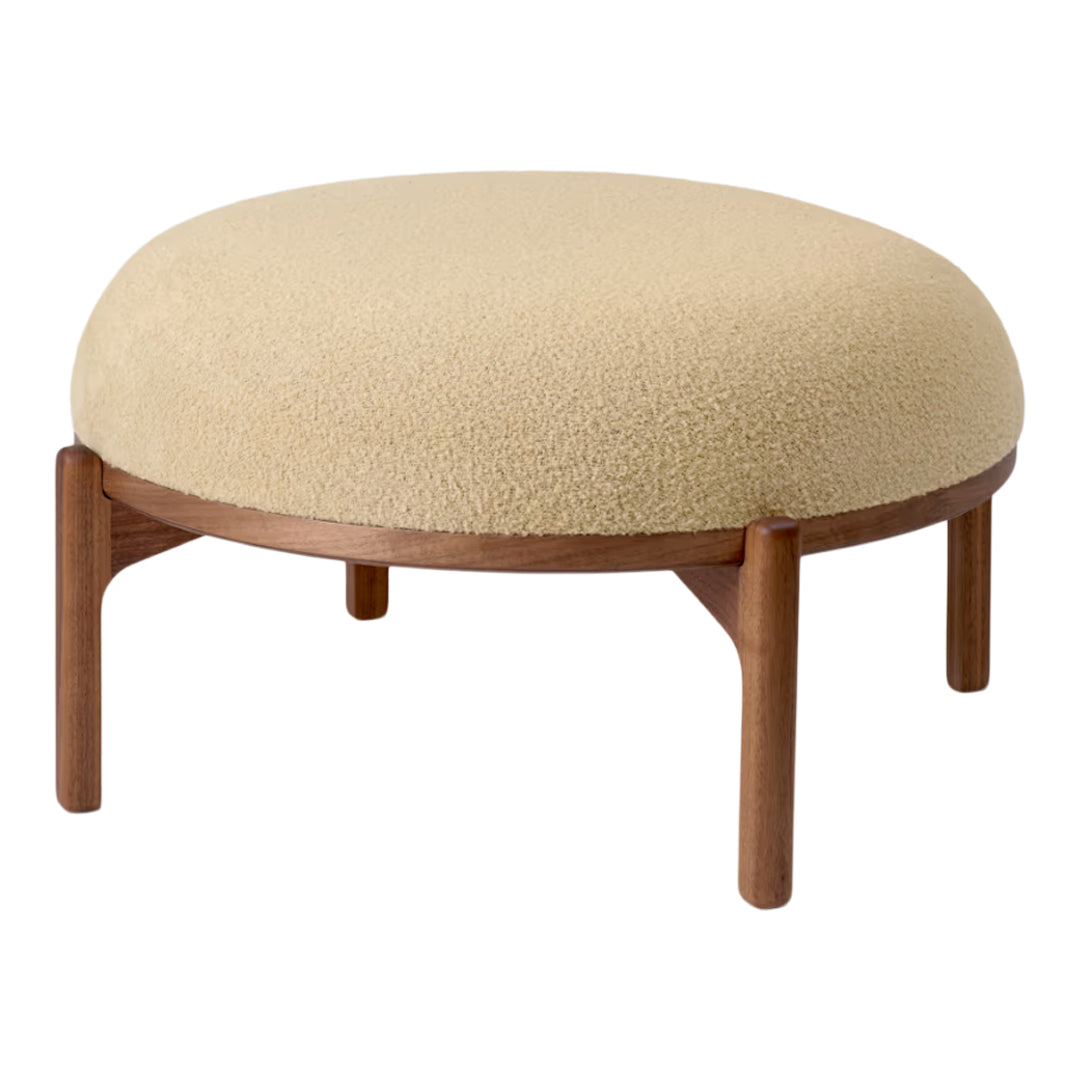 Round beige upholstered ottoman with a soft texture and wooden legs, adding a cozy accent to any room.