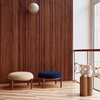 "Beige and navy upholstered ottomans against a wooden slatted wall, with a minimalist round light fixture above."