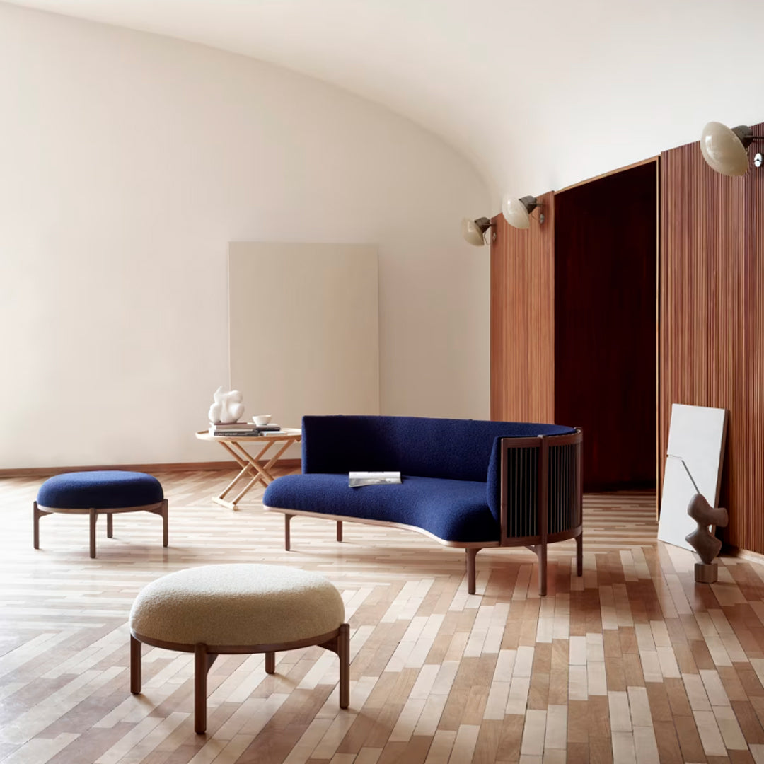 Mid-century modern furniture set featuring a deep blue sofa and cream upholstered stools against warm wooden floors.