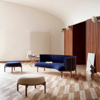 Mid-century modern furniture set featuring a deep blue sofa and cream upholstered stools against warm wooden floors.
