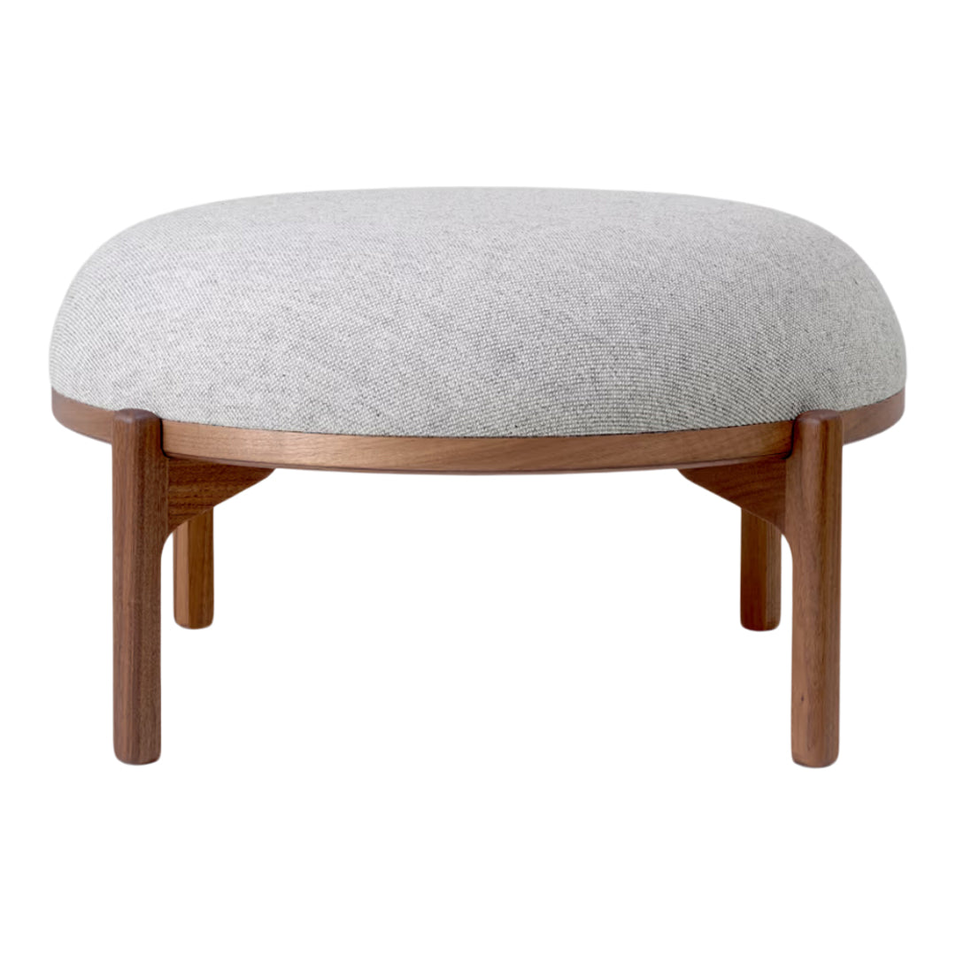Light gray upholstered ottoman with a smooth, rounded top and dark wood legs, featuring a minimalist design.