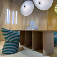 "Colorful striped chair in teal and white with natural wood table and round, textured light fixtures."