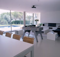 Modern gray foosball table in a bright, minimalist room with white walls and natural light from large windows.