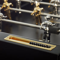 Gold, silver, and black foosball players on a sleek black table with a shiny gold and black control area.