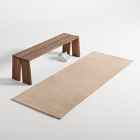 Natural beige area rug with a smooth texture, paired with a minimalist wooden bench in a light wood finish.