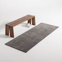 Gray rectangular rug with a subtle texture, paired with a modern wooden bench in a minimalist setting.