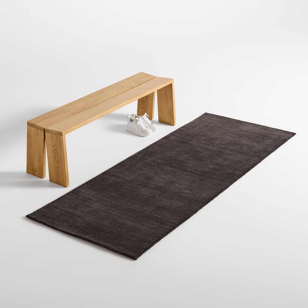 Elegant dark gray rug with subtle texture, paired with a minimalist wooden bench on a clean white background.