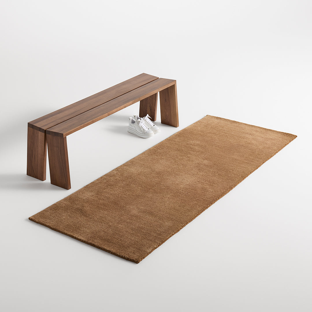 Rust-colored rectangular rug with a smooth texture, paired with a minimalist wooden bench on a neutral background.