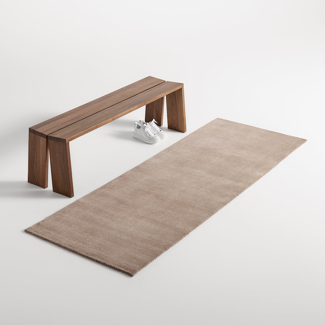 Beige rectangular rug with subtle texture, paired with a light wood bench in a minimalist setting.