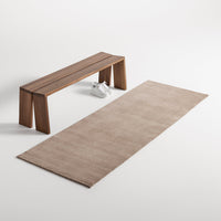 Beige rectangular rug with subtle texture, paired with a light wood bench in a minimalist setting.
