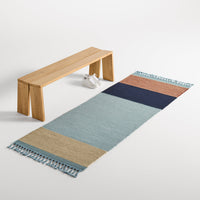 Striped runner rug in soft blue, navy, coral, and natural tones with fringed edges. Perfect for modern decor.