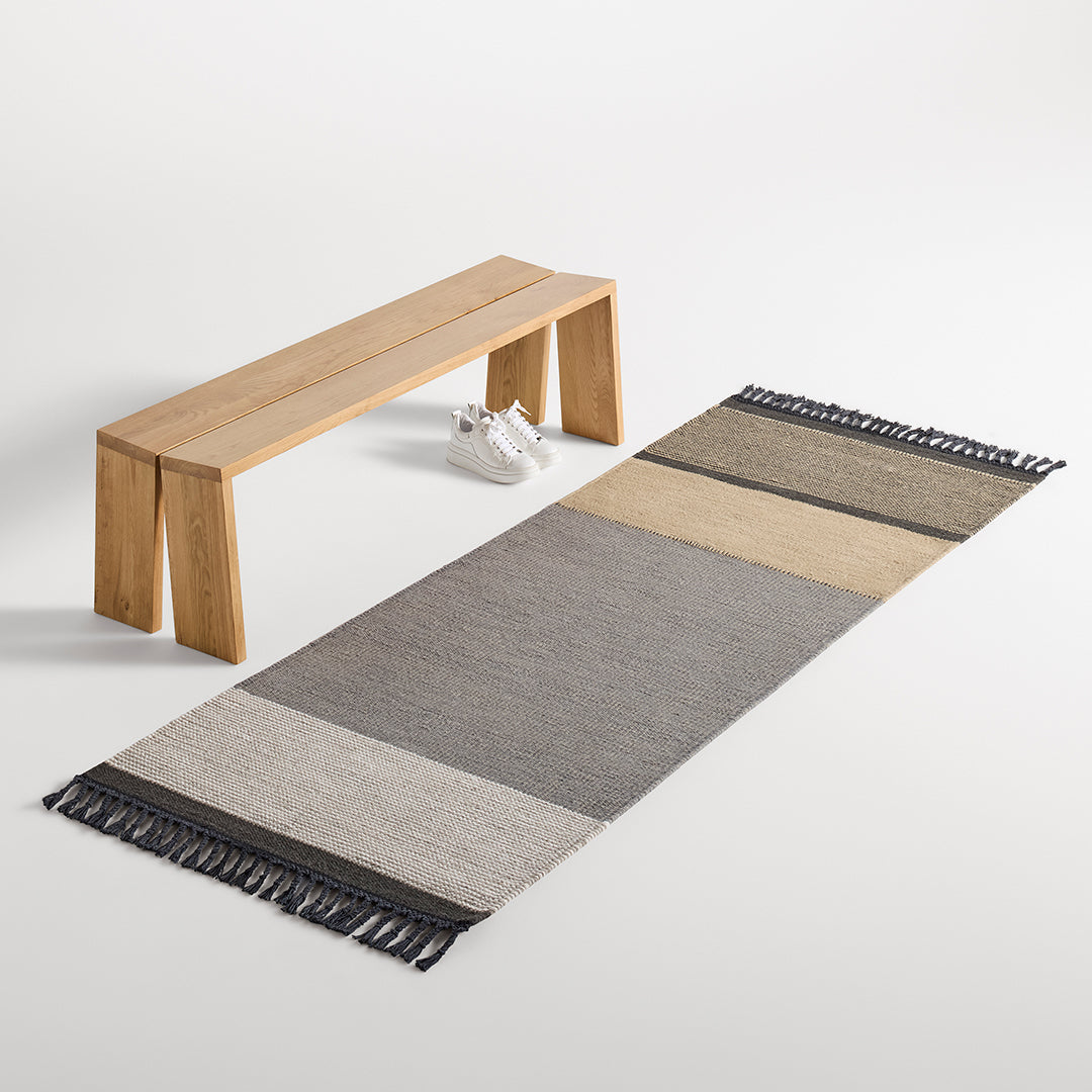 Textured area rug featuring neutral tones of gray, beige, and cream with a striped pattern and fringed edges.