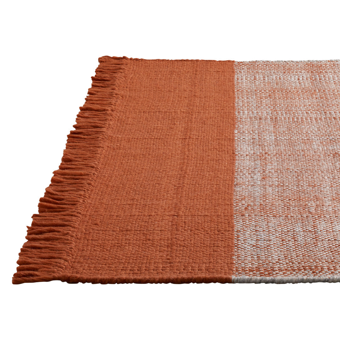 Rust orange and light gray woven rug with textured finish and fringed edges. Perfect for modern home decor.