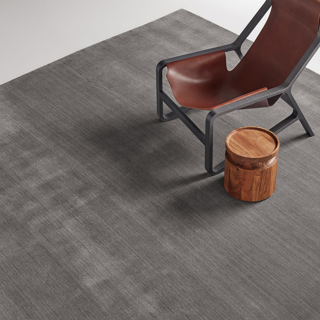Gray patterned rug with subtle textures, paired with a brown chair and wooden stool, creating a modern look.