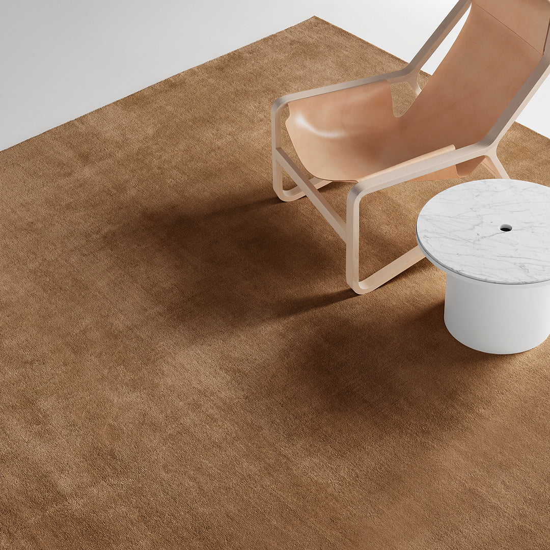 Plain brown area rug with a smooth texture, complementing a light wood chair and a white round table.