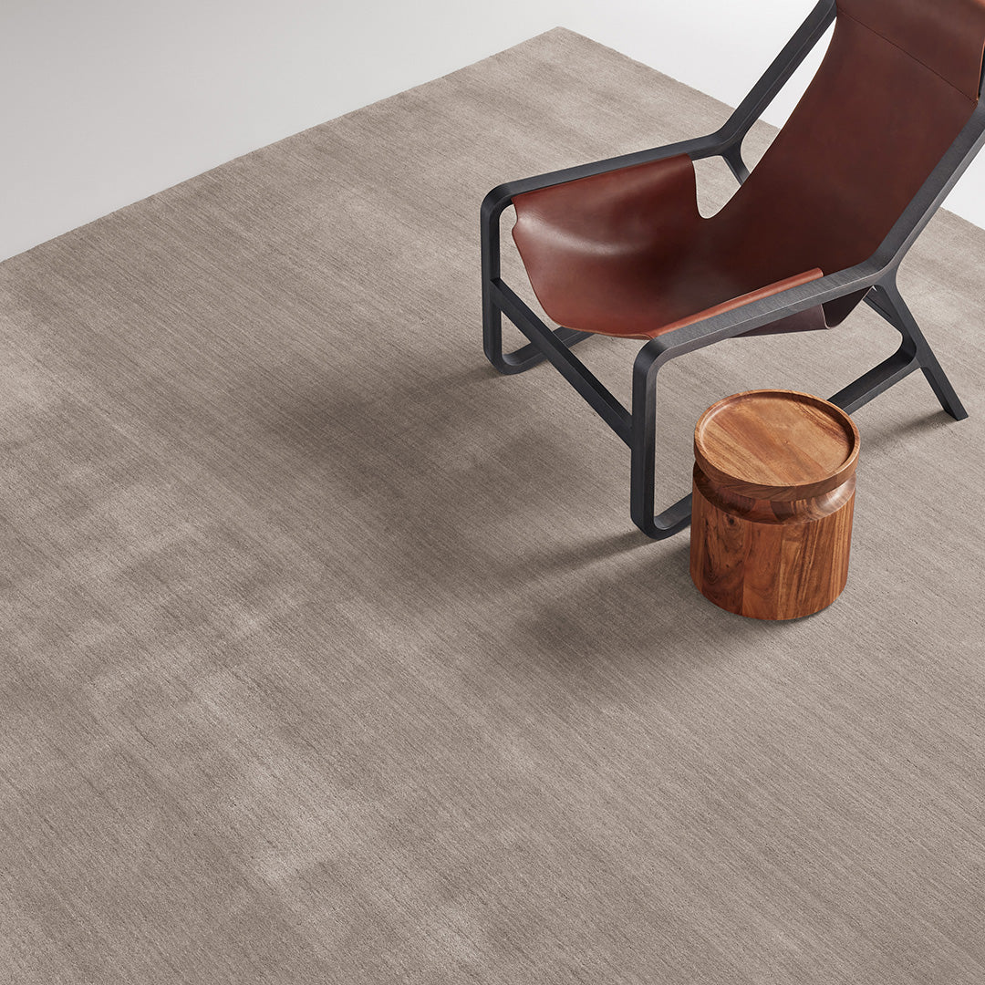 Neutral beige area rug with subtle texture, complemented by a sleek brown chair and wooden stool.