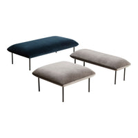 Three upholstered ottomans in dark blue, light gray, and beige with smooth, velvety textures and sleek metal legs.