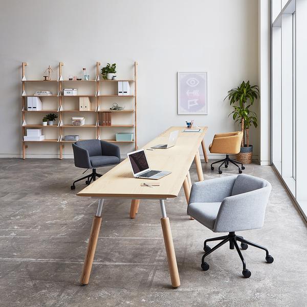 "Contemporary office with light wood table, gray and tan chairs, and natural greenery, featuring a minimalist design."