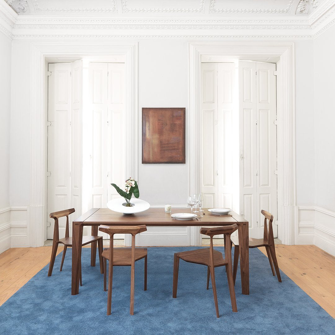 "Elegant wooden dining table set on a light blue rug, complemented by white walls and natural wood tones."