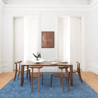 "Elegant wooden dining table set on a light blue rug, complemented by white walls and natural wood tones."