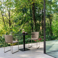 Modern patio setup with neutral woven chairs, a sleek black table, and lush green surroundings in natural sunlight.