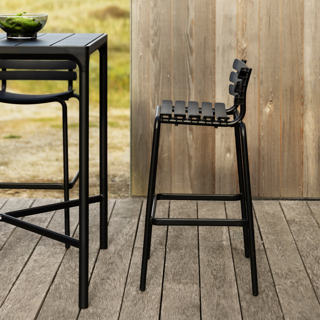 Black slatted bar stool with a sleek design, paired with a matching black table on a wooden deck backdrop.