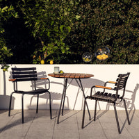 Black metal outdoor chairs with wooden accents, complemented by a round wooden table on a sunny patio.