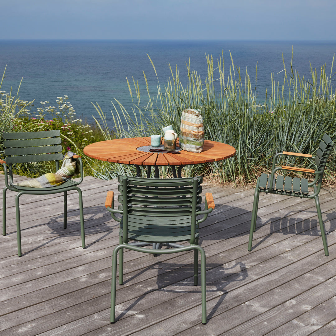 Outdoor dining set featuring a rustic wooden table, green metal chairs, and natural coastal colors against a serene backdrop.