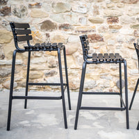 Black bar stools with slatted backs against a textured stone wall, showcasing a modern and minimalist design.