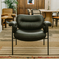 Black leather chair with rounded, plush arms and a minimalist metal frame, set against a patterned rug.