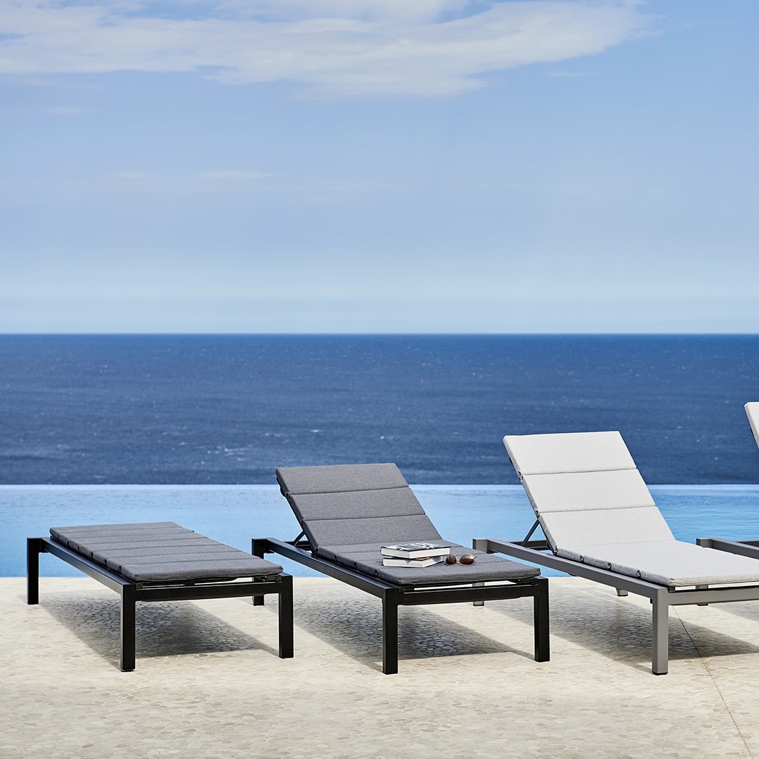 Black and gray loungers with sleek lines against a stunning blue ocean and clear sky backdrop.