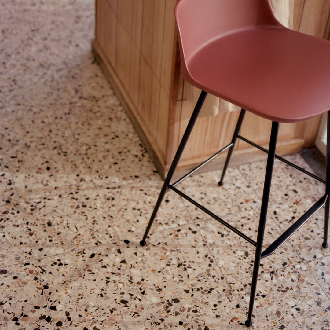 Pink bar stool on textured terrazzo floor with neutral tones and speckled patterns. Modern and stylish dining decor.