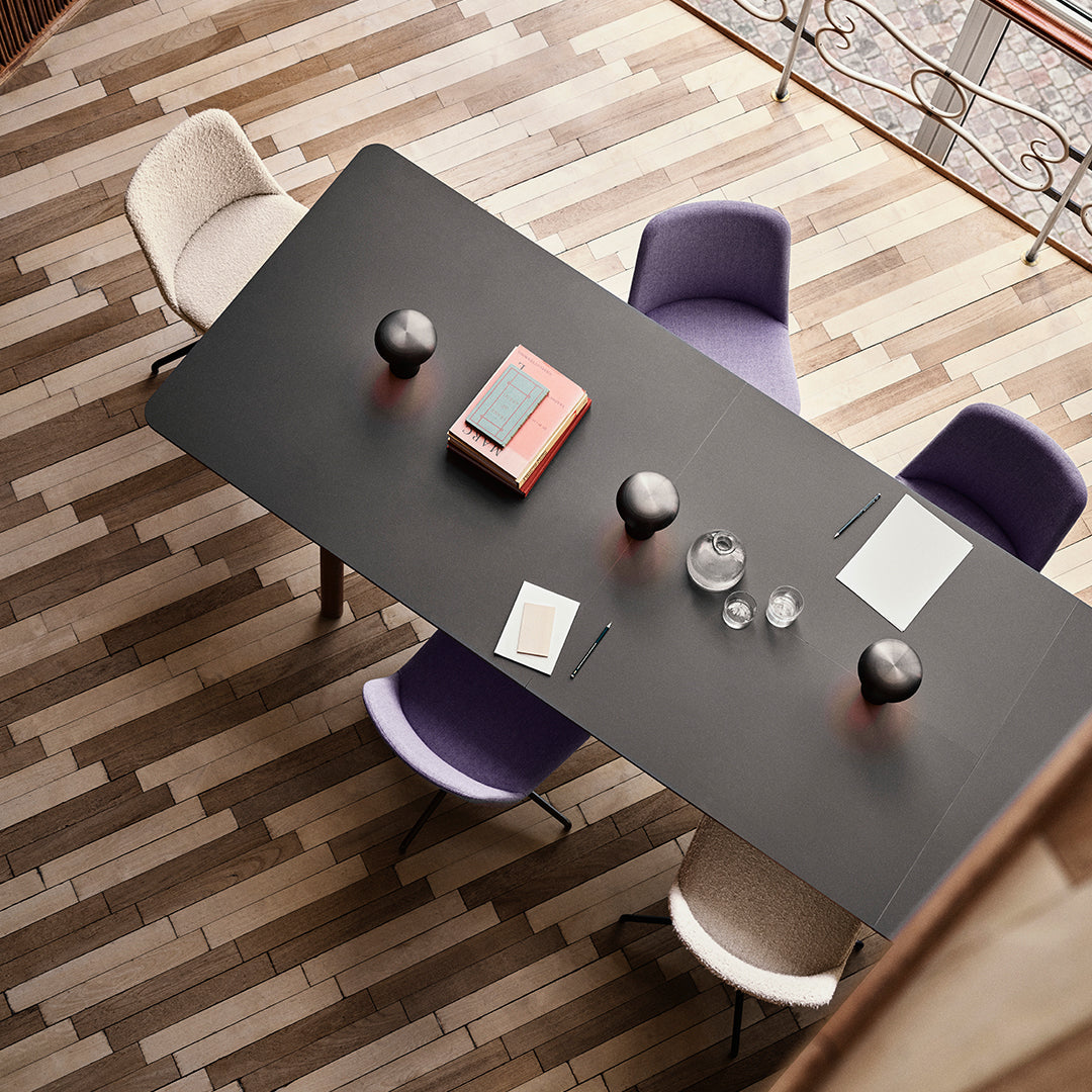 Modern black dining table with lavender and cream chairs, set on a textured brown herringbone floor.
