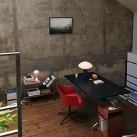 Modern office with a black desk, red chair, and wooden flooring; minimalist decor against a concrete wall.