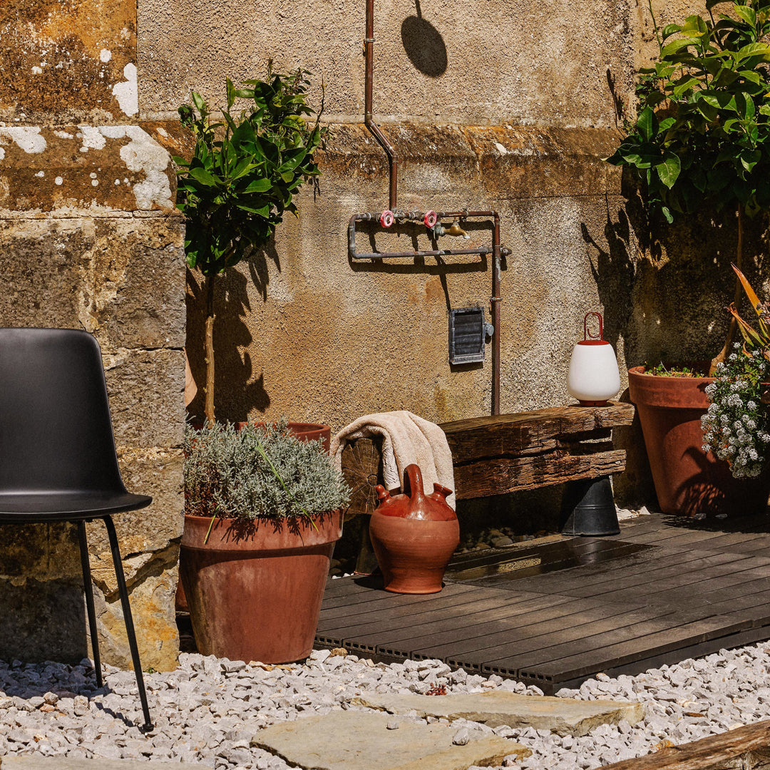 Black chair beside terracotta pots with green plants, rustic wood bench, and neutral tones in a natural outdoor setting.