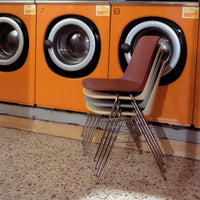 Stacked chairs in muted brown and cream against a vibrant orange backdrop of retro washing machines.
