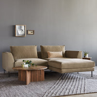 Beige sectional sofa with subtle texture, paired with a natural wood coffee table against a gray backdrop and patterned rug.
