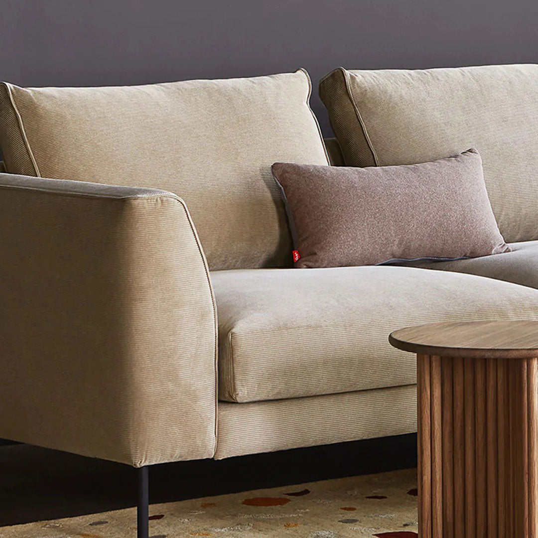 Light beige fabric sofa with a textured brown accent pillow and a warm-toned patterned rug. Modern and cozy design.